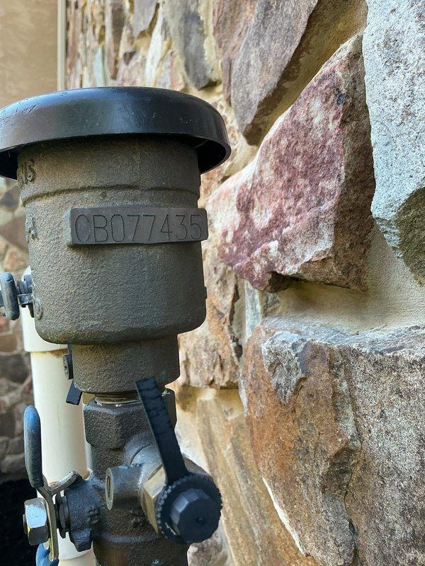 Completed annual backflow prevention device testing on exterior-mounted RPZ assembly. Performed standard five-point test procedure to verify proper operation of check valves, relief valve, and differential pressure across the assembly. Unit CB07435 tested within acceptable parameters and maintained required air gap protection. Documented device condition with photographic evidence showing proper mounting configuration on stone exterior wall with white PVC piping connections. All components functioning correctly with no leaks or deficiencies observed.