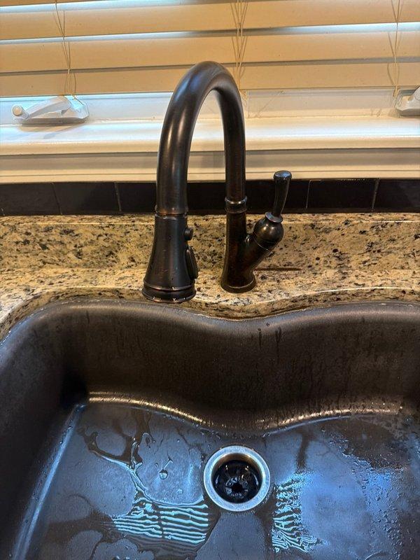 Responded to service call for water leak beneath kitchen sink. Upon arrival, performed diagnostic inspection of plumbing connections and supply lines under sink cabinet. Inspected shut-off valves, P-trap assembly, and all visible water supply connections for signs of active leaking or moisture damage. Examined the installation area including adjacent mechanical systems and structural components in the confined space below the sink. Verified proper operation of kitchen faucet with high-arc spout and side spray attachment. Documented existing conditions with photographs showing plumbing infrastructure, supply lines, and sink fixture installation. Identified source of reported leak and assessed surrounding areas for water damage or compromised connections.