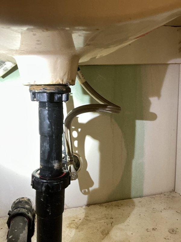 Responded to service call regarding suspected sewer gas odor affecting indoor air quality, with customer reporting respiratory irritation, eye and skin discomfort, and oily residue on walls. Conducted comprehensive inspection of plumbing system including bathroom stack, basement piping, and drain assemblies after fire department and gas company ruled out carbon monoxide and natural gas leaks. Documented existing conditions with photographs showing attic/crawl space plumbing infrastructure with PVC vent stack penetrations through structural framing, and under-sink drain assembly with visible water staining and discoloration on basin underside. Inspection revealed potential drain trap seal failure or compromised vent stack connections that could allow sewer gases to enter living space. Recommended further diagnostic testing of vent stack integrity and potential professional air quality assessment to identify source of reported symptoms and oily deposits.