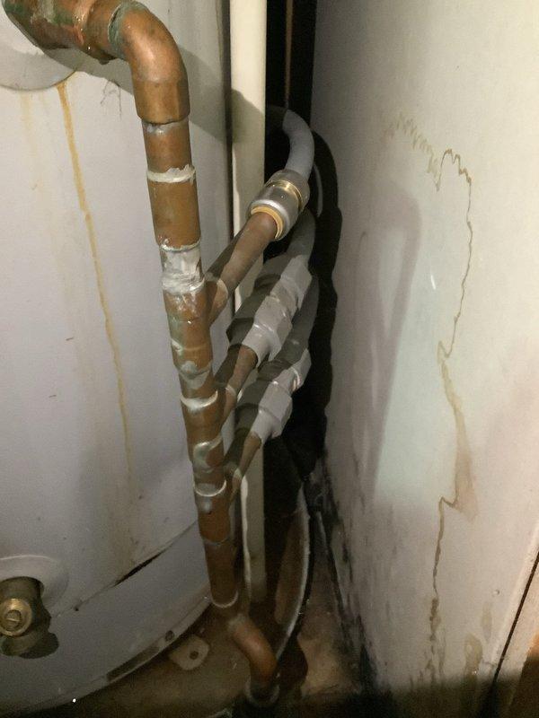 Responded to service call for active water leak originating from top of tanked water heater in 1978 manufactured home. Upon arrival, inspected unit and confirmed leak at top connections with visible water damage and staining on surrounding walls indicating prolonged moisture exposure. Assessed gas control valve, flexible gas connectors with brass fittings, and PVC venting system for proper operation and code compliance. Evaluated copper supply lines showing oxidation and previous repair attempts with tape wrapping. Determined extent of corrosion on piping and water heater components. Documented condition of installation including deteriorated wall surfaces with water staining and spotting consistent with chronic leak issues. Provided assessment and recommendations for repair versus replacement options given age of home and existing plumbing infrastructure.