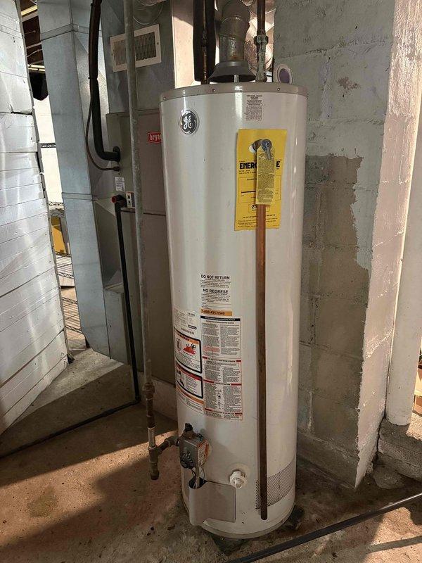 Conducted comprehensive HVAC system evaluation for residential property in preparation for home sale. Assessed existing outdoor air conditioning condenser unit located in side yard utility access area and inspected GE water heater installation in basement utility room, documenting current equipment conditions and specifications to develop replacement estimate quotes for both cooling system addition and complete HVAC system upgrade.