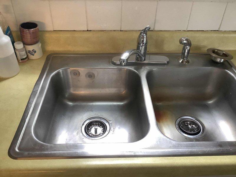 Replaced kitchen faucet with new single-handle unit including side spray assembly. Installed two new basket strainers in double-basin stainless steel sink. Replaced center outlet waste assembly, P-traps, and associated drain piping under both sink compartments with new PVC components to ensure proper drainage and code compliance.
