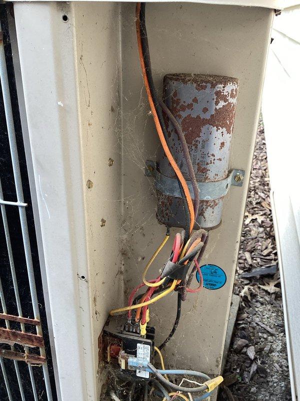 Responded to no cooling complaint on aging residential air conditioning system. Upon arrival, performed diagnostic inspection of outdoor condensing unit. Found severely corroded dual run capacitor with significant rust damage affecting electrical connections. The capacitor showed brown and orange discoloration indicating advanced deterioration from prolonged outdoor exposure. Inspected associated electrical components including contactor and wiring connections. Due to the age of the unit (over 10 years) and advanced corrosion of critical electrical components, documented equipment condition with photos showing the failed capacitor, deteriorated wiring connections, and overall weathering of the outdoor unit cabinet and coil assembly.