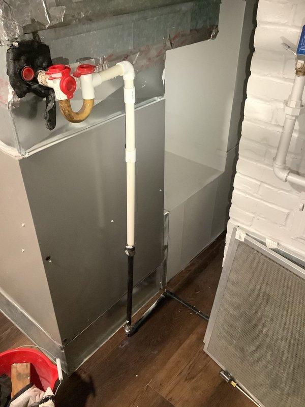 Responded to service call for blocked condensate line in 75-year-old residential property. Upon inspection, located HVAC air handler unit in basement utility area with white PVC condensate drain lines running vertically alongside the system. Cleared blockage from condensate line to restore proper drainage function and prevent potential water damage or system shutdown. Verified proper flow through drain trap and confirmed all plumbing connections were secure, including copper piping with U-trap configuration in the mechanical room area. System tested and returned to normal operation with condensate draining freely.