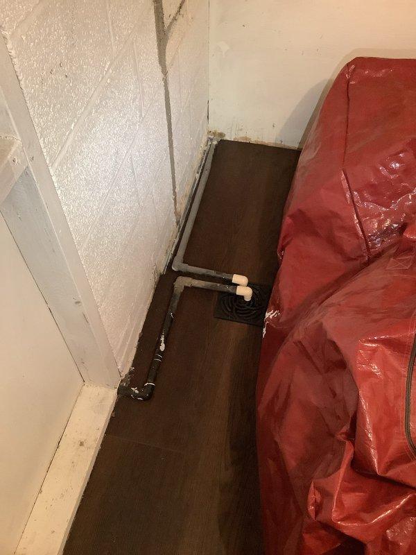 Responded to service call for blocked condensate line in 75-year-old residential property. Upon inspection, located HVAC air handler unit in basement utility area with white PVC condensate drain lines running vertically alongside the system. Cleared blockage from condensate line to restore proper drainage function and prevent potential water damage or system shutdown. Verified proper flow through drain trap and confirmed all plumbing connections were secure, including copper piping with U-trap configuration in the mechanical room area. System tested and returned to normal operation with condensate draining freely.