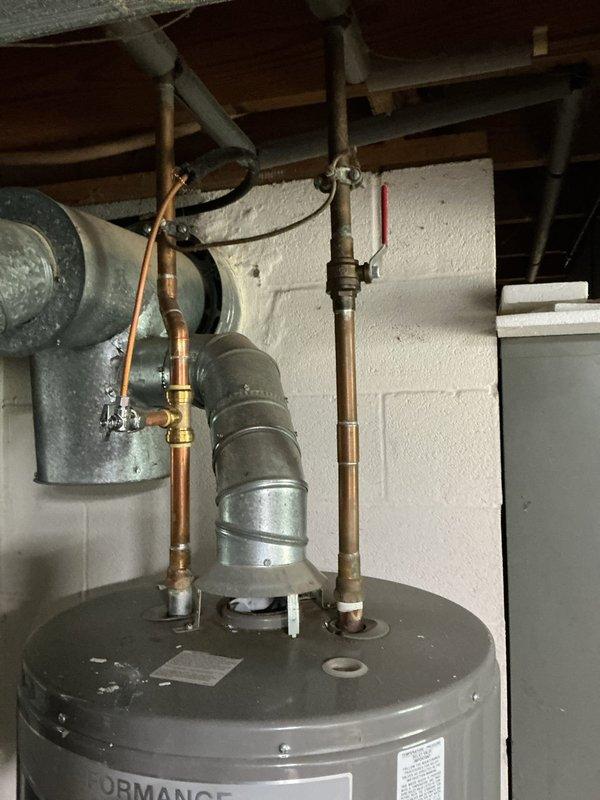 Conducted on-site assessment of a 9-year-old Rheem Performance tanked water heater exhibiting active leakage. Inspected the unit and surrounding plumbing connections, including copper supply lines, brass shut-off valves, pressure relief valve, and associated galvanized ductwork. Documented existing installation configuration with photographs showing tank condition, pipe routing, and mechanical room layout. Provided estimate for complete water heater replacement due to tank failure, as the existing unit had reached the end of its serviceable life and repair was not economically viable.