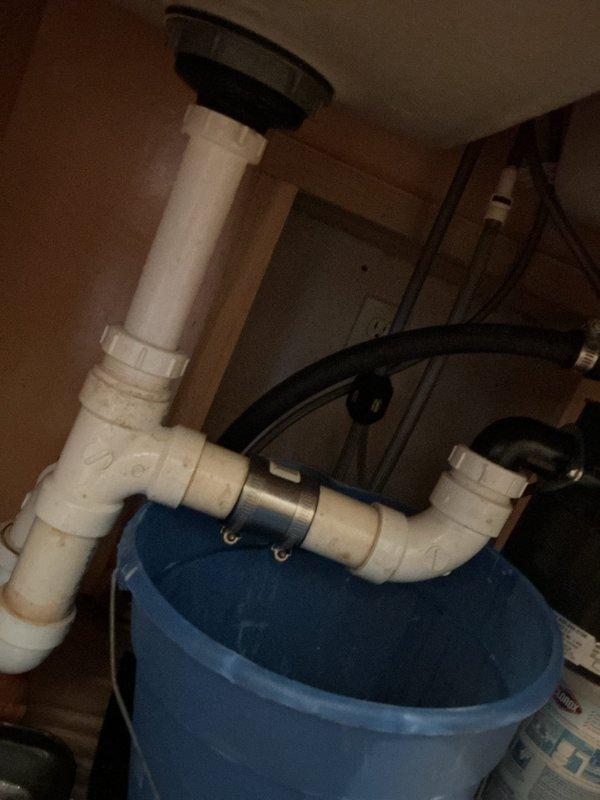 Responded to kitchen drain clog in 28-year-old residence. Upon inspection, located clogged drain line in basement utility area beneath kitchen sink. Identified blockage in PVC trap assembly causing drainage backup and standing water accumulation in drip pan. Cleared obstruction from drain system, flushed lines to restore proper flow, and verified drainage functionality. System tested and operating normally upon completion.