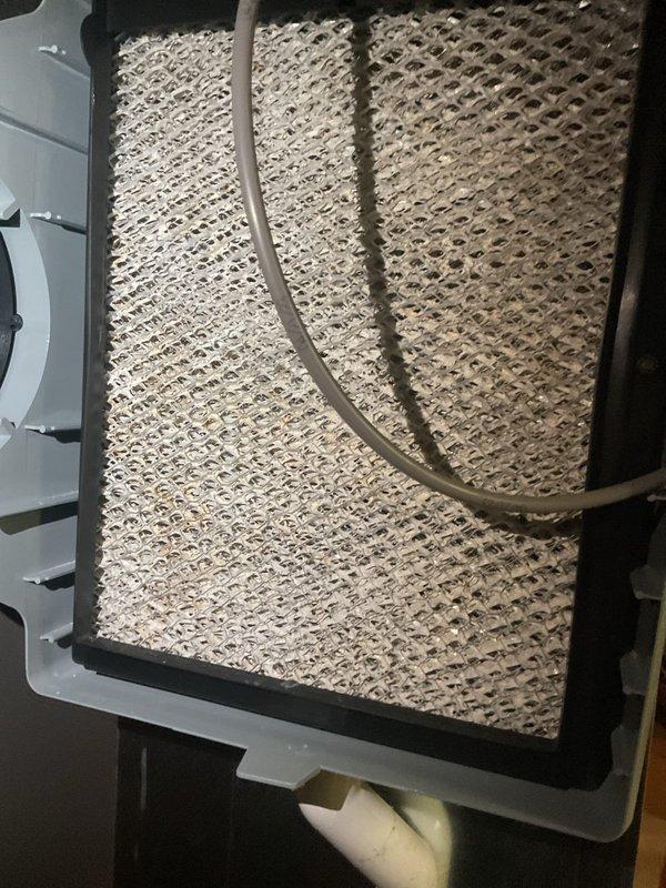 Completed preventive maintenance cooling visit on 2-year-old HVAC system. Inspected and serviced humidifier system, including evaluation of evaporator pad which showed moderate dust accumulation and discoloration requiring monitoring. Verified Aprilaire humidifier control operation with digital display reading 59% and confirmed proper functionality of control dial and indicator lights.