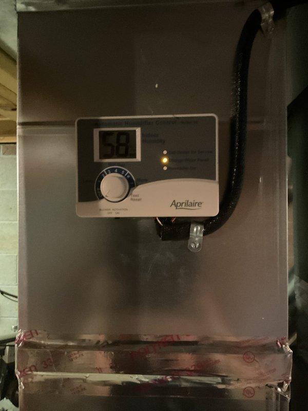 Completed preventive maintenance cooling visit on 2-year-old HVAC system. Inspected and serviced humidifier system, including evaluation of evaporator pad which showed moderate dust accumulation and discoloration requiring monitoring. Verified Aprilaire humidifier control operation with digital display reading 59% and confirmed proper functionality of control dial and indicator lights.