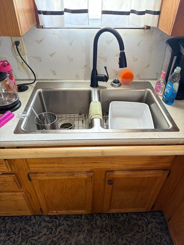 Conducted on-site assessment of kitchen sink and plumbing system to provide estimate for sink removal and reinstallation services. Inspected double-basin stainless steel sink with matte black pull-down faucet, documented existing plumbing configuration including white PVC P-trap assembly, black garbage disposal unit with connection hoses, and under-cabinet storage arrangement. Photographed current installation to provide accurate scope of work for future service scheduling.