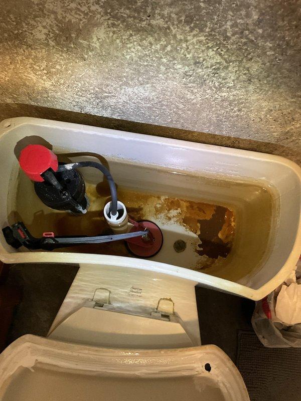 Responded to complaint of continuously running toilet. Upon inspection, found toilet tank fill valve failing to shut off properly, causing constant water flow into overflow tube. Tank interior showed extensive rust staining, mineral deposits, and corroded components affecting flush mechanism performance. Diagnosed faulty fill valve assembly and worn flapper valve as primary causes of running condition. Documented existing corrosion and deterioration of internal tank components for repair recommendations.
