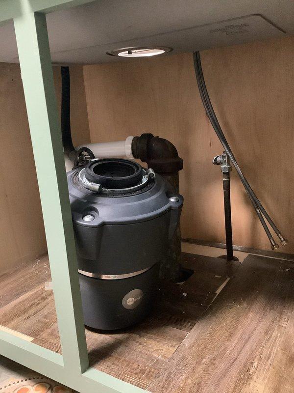 Completed installation of kitchen sink plumbing system including undermount stainless steel sink with polished stone countertop integration, oil-rubbed bronze gooseneck faucet with side lever handle, and black garbage disposal unit with associated drainage piping and connections. All components were properly mounted, secured, and tested for proper operation and leak-free performance.