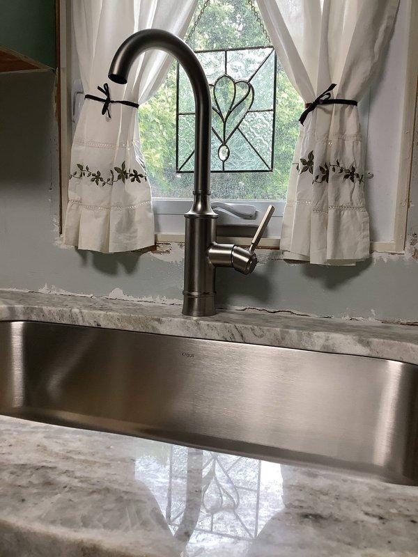 Completed installation of kitchen sink plumbing system including undermount stainless steel sink with polished stone countertop integration, oil-rubbed bronze gooseneck faucet with side lever handle, and black garbage disposal unit with associated drainage piping and connections. All components were properly mounted, secured, and tested for proper operation and leak-free performance.