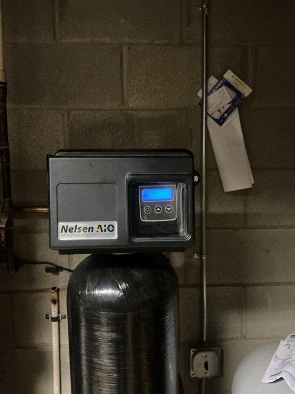 Responded to service call for malfunctioning Nelsen water softener system displaying error code and flashing display. Upon arrival, inspected the unit and found the system showing 1121 gallons of remaining capacity on the digital control head. Diagnosed electrical power supply issue causing the intermittent flashing condition. Tested system connections, verified proper operation of the control valve, and confirmed water flow through the copper supply lines. Reset the control head programming to restore normal operation. System tested and returned to full working order with proper regeneration cycle functionality.