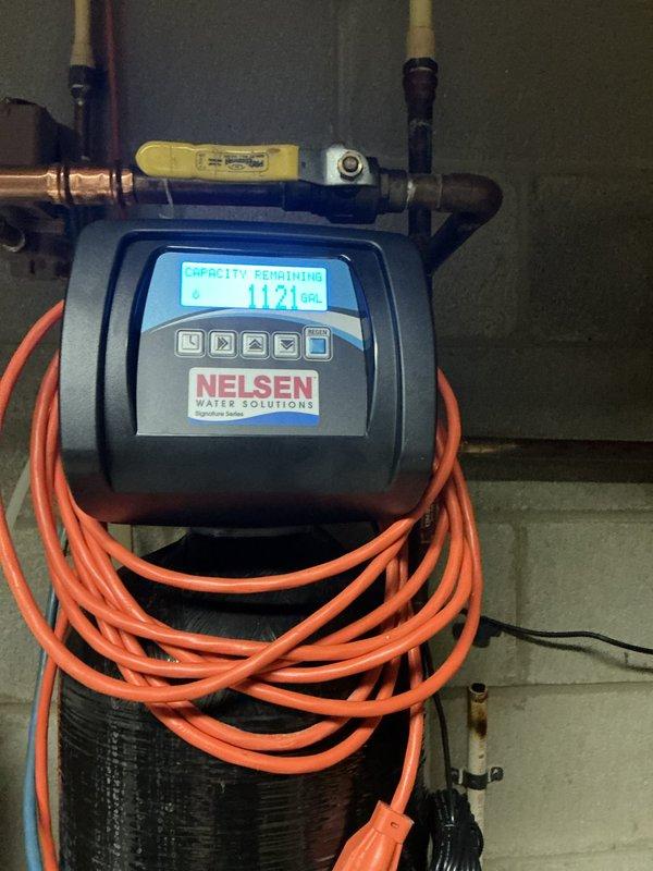 Responded to service call for malfunctioning Nelsen water softener system displaying error code and flashing display. Upon arrival, inspected the unit and found the system showing 1121 gallons of remaining capacity on the digital control head. Diagnosed electrical power supply issue causing the intermittent flashing condition. Tested system connections, verified proper operation of the control valve, and confirmed water flow through the copper supply lines. Reset the control head programming to restore normal operation. System tested and returned to full working order with proper regeneration cycle functionality.