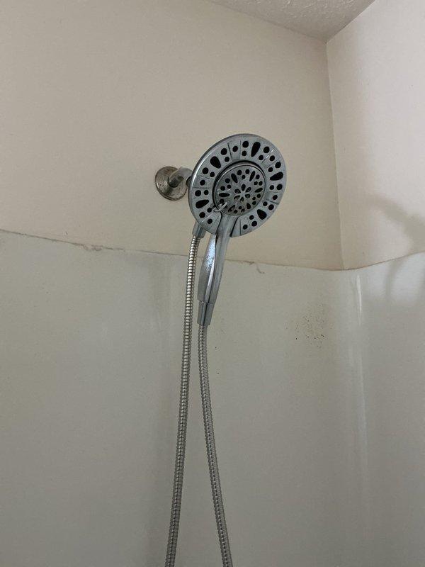 Installed customer-supplied Moen Renewal handheld shower head assembly with wall bracket and flexible metal hose in bathroom shower/tub area. Verified proper mounting, connection integrity, and functionality of the new fixture upon completion.