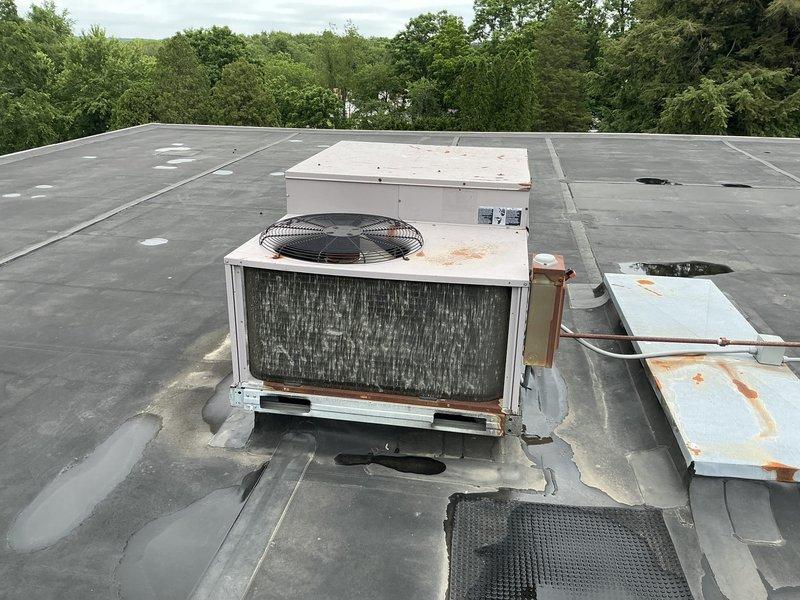 Completed site assessment for replacement of two rooftop commercial HVAC units at school facility. Both packaged rooftop units dating from 1999 showed significant deterioration including extensive rust staining on exterior panels, aged and darkened internal coils, and one unit experiencing freezing issues. Documentation revealed water pooling around unit bases with visible membrane staining, weathered components, and compromised operational efficiency. Photographed existing equipment conditions, copper refrigerant line routing, roof penetrations, and curb adapter configurations to facilitate accurate replacement specifications and ensure proper coordination for summer installation during optimal 10 AM-2 PM timeframe when roof access is unobstructed.