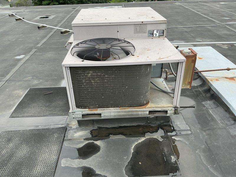 Completed site assessment for replacement of two rooftop commercial HVAC units at school facility. Both packaged rooftop units dating from 1999 showed significant deterioration including extensive rust staining on exterior panels, aged and darkened internal coils, and one unit experiencing freezing issues. Documentation revealed water pooling around unit bases with visible membrane staining, weathered components, and compromised operational efficiency. Photographed existing equipment conditions, copper refrigerant line routing, roof penetrations, and curb adapter configurations to facilitate accurate replacement specifications and ensure proper coordination for summer installation during optimal 10 AM-2 PM timeframe when roof access is unobstructed.