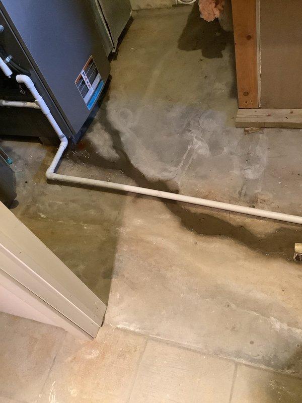 Responded to service call for water draining onto floor instead of through drain pipe. Upon inspection, found standing water in PVC condensate drain line and extensive water pooling on basement floor around HVAC unit. Identified drainage issue with condensate system causing water to overflow onto concrete surface rather than properly evacuating through drain piping. Documented conditions showing water accumulation in drain line and moisture damage on floor surrounding equipment.