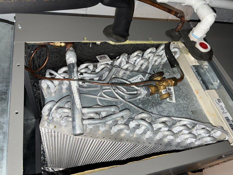 Responded to service call for thermostat malfunction with system stuck in heating mode. Upon inspection, discovered evaporator coil completely frozen with extensive ice buildup covering the entire coil assembly. Diagnosed root cause as airflow restriction preventing proper heat exchange, causing coil temperature to drop below freezing point. Shut down system to allow coil to thaw completely. Identified thermostat was functioning properly but system had been running continuously in cooling mode rather than heating mode as customer believed, resulting in freeze condition. Verified refrigerant lines, connections, and copper tubing condition. Once thaw completed, checked drain pan for proper condensate drainage. Educated customer on proper thermostat operation and difference between heating and cooling modes to prevent future confusion.