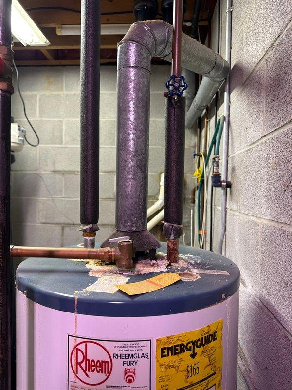 Conducted on-site assessment and provided quote for complete water heater replacement and water treatment system upgrade. Evaluated existing Rheem Rheemglas Fury tank-style water heater showing significant corrosion and mineral deposits on top lid and around pipe connection points, indicating advanced deterioration and potential system failure. Assessed current plumbing configuration including copper supply lines, vertical piping with valve controls, and existing venting system. 

Inspected existing water treatment system consisting of two black cylindrical filters mounted in series to floor joists via copper piping connections. Evaluated filter condition, mounting hardware, and integration with main water supply lines running along concrete block foundation wall. Documented all components including valve assemblies, pipe routing, and connection points to determine scope of necessary upgrades for improved water quality and system performance. Provided comprehensive replacement recommen