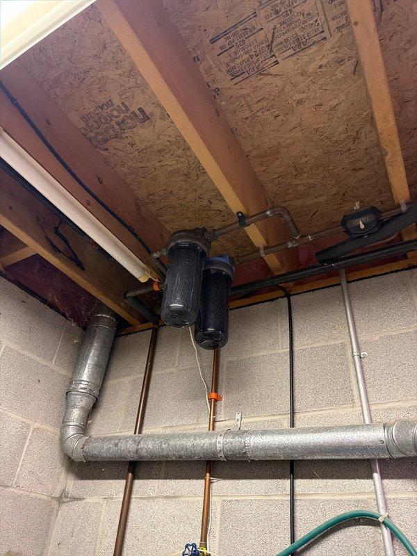Conducted on-site assessment and provided quote for complete water heater replacement and water treatment system upgrade. Evaluated existing Rheem Rheemglas Fury tank-style water heater showing significant corrosion and mineral deposits on top lid and around pipe connection points, indicating advanced deterioration and potential system failure. Assessed current plumbing configuration including copper supply lines, vertical piping with valve controls, and existing venting system. 

Inspected existing water treatment system consisting of two black cylindrical filters mounted in series to floor joists via copper piping connections. Evaluated filter condition, mounting hardware, and integration with main water supply lines running along concrete block foundation wall. Documented all components including valve assemblies, pipe routing, and connection points to determine scope of necessary upgrades for improved water quality and system performance. Provided comprehensive replacement recommen