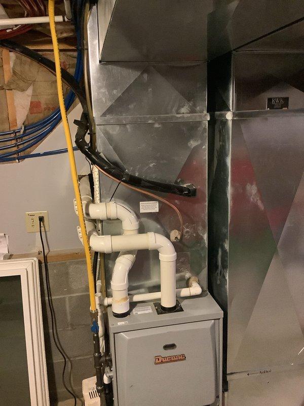 Completed second phase of air conditioning and evaporator coil installation on existing Ducane furnace system. Installed new evaporator coil above furnace unit with proper sheet metal ductwork transitions and verified condensate drainage system connections using white PVC piping configuration. Performed temperature differential testing with calibrated digital instrumentation, confirming system performance at 152°F discharge temperature, indicating proper heat exchange operation and successful integration with existing HVAC infrastructure.