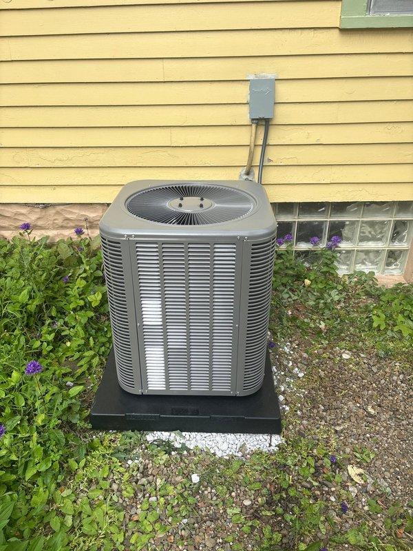 Completed installation of outdoor air conditioning condenser unit with R-454B refrigerant system. Unit was properly mounted on platform base against exterior wall with electrical disconnect box and conduit installed per code requirements. Refrigerant lines were connected to brass valve assembly and routed through unit, with all connections secured and tested for proper operation.
