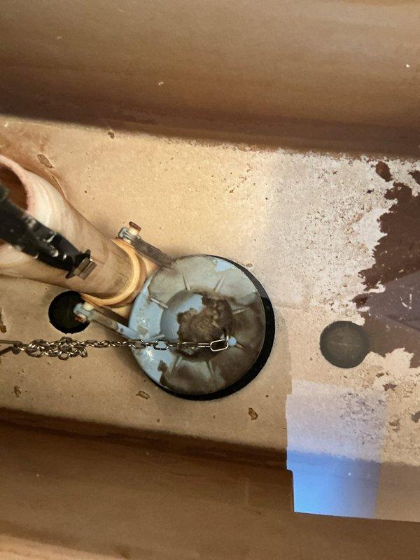 Responded to upstairs toilet that was intermittently running and refilling every five to six hours with low water level in tank. Upon inspection, found deteriorated blue flapper valve with mineral deposits and significant staining throughout tank interior. Flapper was not sealing properly against flush valve seat, causing phantom flushes and continuous water loss. Documented existing conditions showing heavy mineral buildup on tank surfaces and fill valve components. Recommended replacement of flapper assembly and fill valve to restore proper operation and prevent water waste.