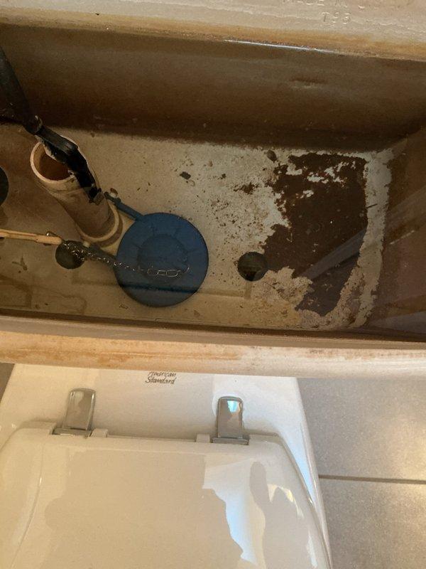 Responded to upstairs toilet that was intermittently running and refilling every five to six hours with low water level in tank. Upon inspection, found deteriorated blue flapper valve with mineral deposits and significant staining throughout tank interior. Flapper was not sealing properly against flush valve seat, causing phantom flushes and continuous water loss. Documented existing conditions showing heavy mineral buildup on tank surfaces and fill valve components. Recommended replacement of flapper assembly and fill valve to restore proper operation and prevent water waste.