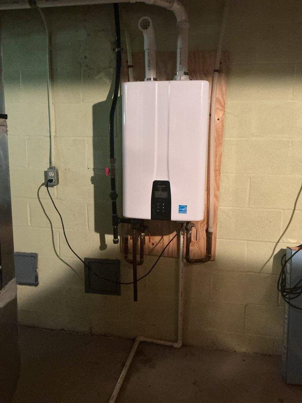 Performed maintenance flush and fill service on wall-mounted tankless water heater unit. Customer inquired about recommended service intervals for ongoing maintenance of the system. Unit is properly mounted on basement utility room wall with organized copper piping and gas line connections, displaying Energy Star certification and functioning digital control panel.