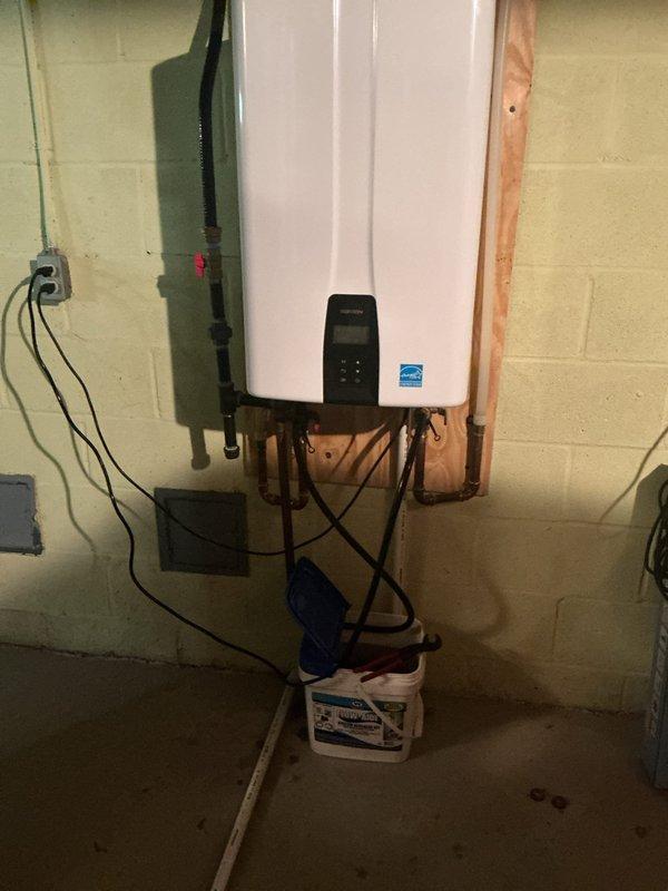 Performed maintenance flush and fill service on wall-mounted tankless water heater unit. Customer inquired about recommended service intervals for ongoing maintenance of the system. Unit is properly mounted on basement utility room wall with organized copper piping and gas line connections, displaying Energy Star certification and functioning digital control panel.