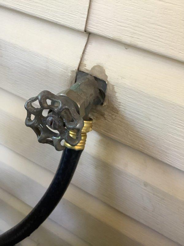 Responded to outdoor faucet leak on white vinyl siding. Upon inspection, found brass hose bib with significant water staining and discoloration around pipe penetration point, indicating active leak at wall connection. Documented existing damage to siding from prolonged water exposure. Assessed fixture condition and determined replacement necessary due to failed seal at mounting point. Photographed evidence of leak damage for customer review and estimate preparation.