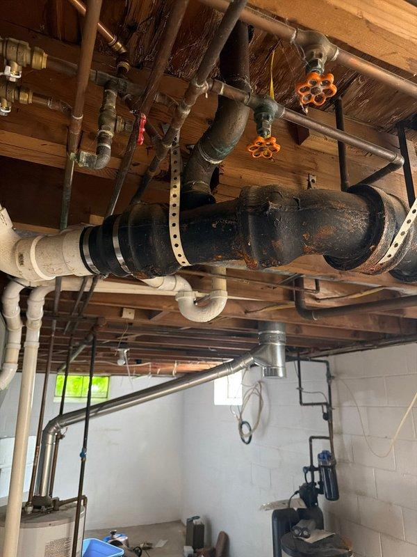 Responded to service call for cracked pipe in basement. Upon inspection, discovered severely corroded and deteriorated metal piping system in utility room area above washing machine. The existing pipe exhibited extensive rust, oxidation, and structural compromise throughout, with flaking metal and significant corrosion damage that created failure points in the system. Documented conditions with photographs showing the extent of deterioration to both the main cylindrical ductwork/piping and associated plumbing infrastructure mounted to ceiling joists. Assessed surrounding copper, PVC, and metal pipe connections, valves, and mounting hardware for related damage. Provided estimates for pipe replacement and repair options to address the compromised plumbing system.