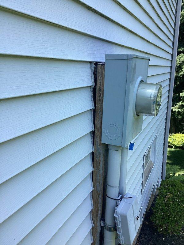 Responded to service call for electrical panel mounting concern. Upon inspection, found electrical meter housing and panel mounted to backing board that was separating from exterior wall, allowing water infiltration behind assembly. Documented existing conditions with photographs showing meter socket, PVC conduit installation, and deteriorated wooden backing support. Exterior assessment completed and findings reported to property contact for repair authorization.