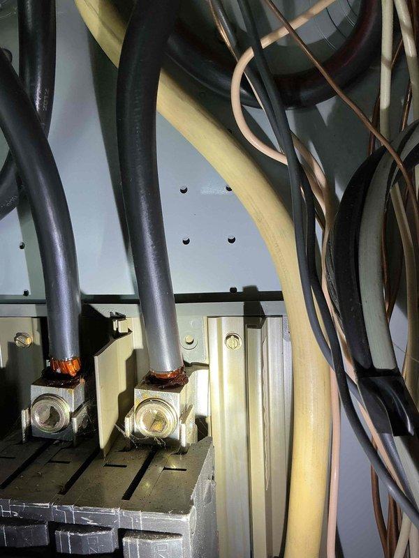 # Electrical Service - Panel/Breakers

Responded to service call for air conditioning unit repeatedly tripping breaker at residential property with 21-year-old electrical panel. Upon arrival, conducted visual inspection of exterior-mounted electrical service panel and associated wiring connections.

## Inspection Findings

Examined main electrical panel box mounted on exterior wall with wood shake siding. Inspected panel cover, conduit connections, and overall panel condition given the age of the installation. Opened panel to assess internal components including breaker arrangement, wire terminations, and bus bar connections.

Observed multiple cable entries at top of panel with various conduit types including rigid metal conduit with compression fittings. Noted complex wire routing with multiple circuits in various colors (black, green, copper, beige, yellow) typical of older residential installations. Identified brass/bronze termination fittings with visible copper conductor strands 