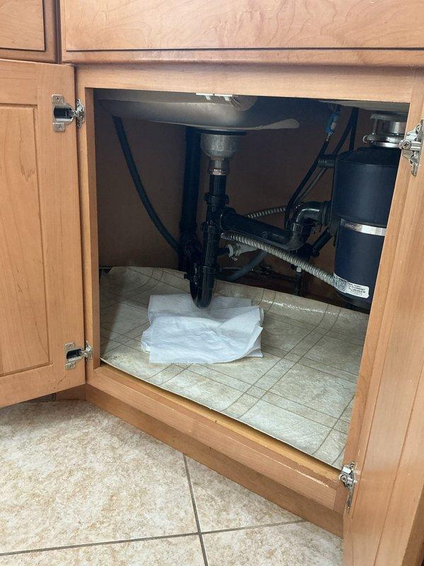Responded to water leak complaint affecting kitchen sink and utility sink. Upon inspection, identified leaking connections at P-trap assembly and supply line fittings beneath kitchen sink cabinet. Tightened threaded connections on P-trap where it joins the sink drain tailpiece. Inspected flexible braided supply lines and angle stop valves, noting mineral deposits and age-related deterioration on shut-off valve components. Verified garbage disposal connections and drain assembly for proper sealing. Placed absorbent materials beneath plumbing fixtures as precautionary measure during inspection and repair. Tested all connections for leaks and confirmed water-tight seals upon completion.