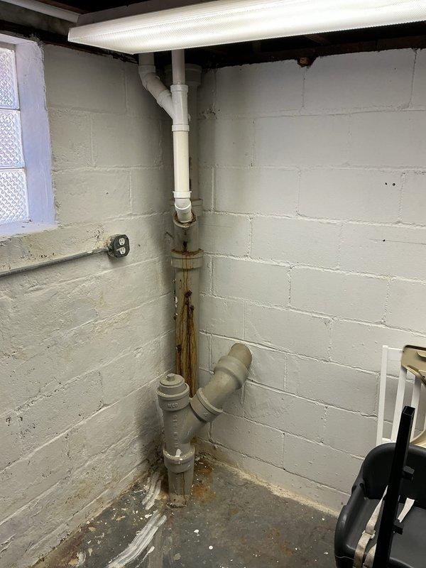 Responded to main line drainage issue where flushing the upstairs toilet caused air bubbles and splashing in the downstairs toilet. Upon inspection, identified significant rust staining on basement plumbing assembly indicating long-term deterioration of metal piping sections. Assessed drainage system configuration including PVC and aging metal pipe connections, gray PVC trap junction, and corrugated drainage lines. Documented existing plumbing conditions showing water-related deterioration at pipe connections and recommended monitoring for potential backflow issues given the cross-fixture symptoms indicating partial main line obstruction.