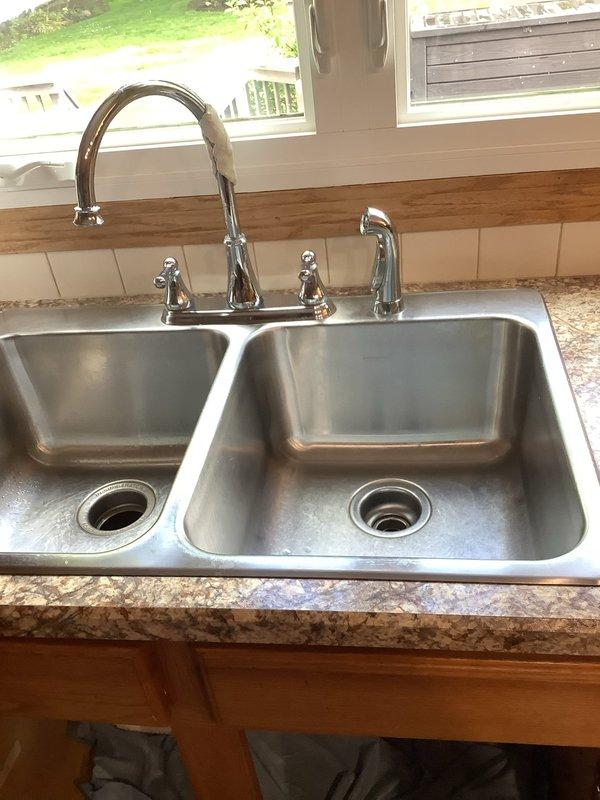 Installed customer-supplied stainless steel kitchen sink and chrome faucet assembly in granite countertop. Reconnected existing garbage disposal unit to new sink drain configuration and installed new drain piping to accommodate updated fixture layout. All connections tested and verified operational with no leaks detected.