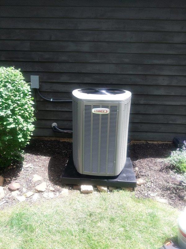 Completed full HVAC system installation including indoor air handler unit positioned in upstairs utility closet and outdoor Lennox condenser unit. Air handler properly mounted with PVC condensate drain lines, refrigerant line sets, and electrical connections secured via flexible conduit. Outdoor condenser installed on concrete pad against building exterior with proper clearances, refrigerant lines and electrical conduit professionally routed through weather-protected junction box into building. System tested and verified operational at 90% completion stage with final startup procedures pending.