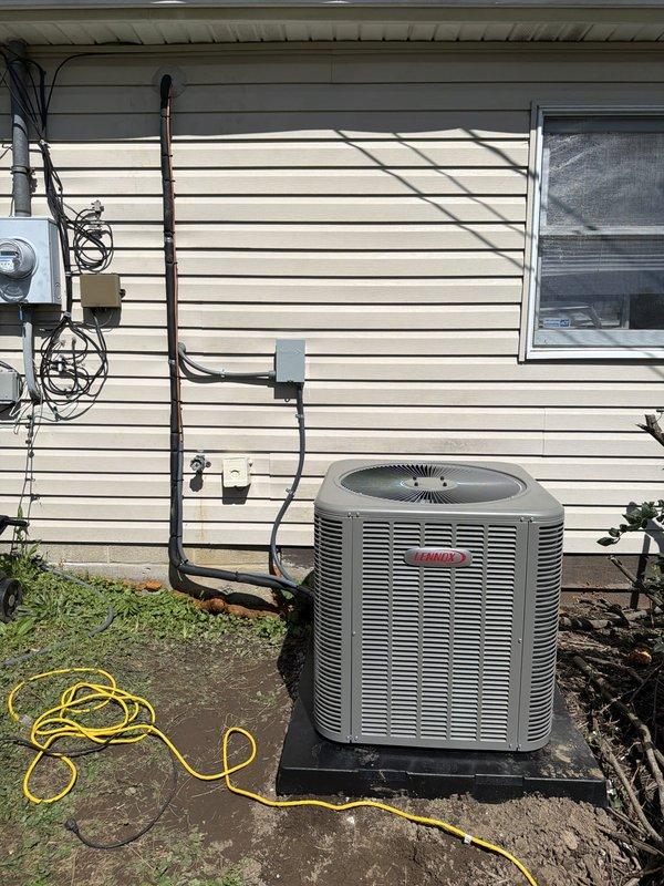 Completed installation of 80% efficiency furnace and air conditioning system at residential property. New outdoor condensing unit was positioned on pad against exterior wall with proper clearance, refrigerant lines were run and insulated along siding to interior connection point, and electrical disconnect box was mounted per code requirements. System was tested and confirmed operational upon completion.