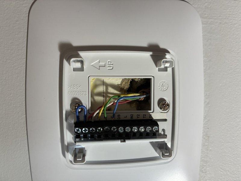 Responded to service call for non-functioning Aprilaire thermostat following recent PCB installation. Inspected thermostat wiring connections at wall-mounted control device, verified proper wire terminations at numbered terminal block, and confirmed thermostat display was operational showing 73° with system in cooling mode and fan set to auto. Documented wiring configuration and thermostat functionality with photos for service records.