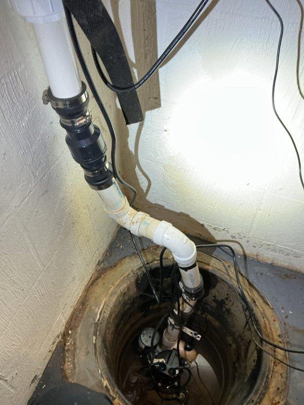 Installed new discharge line for sump pump battery backup system in basement utility area. Work included running white PVC piping with proper fittings and securing to wall with metal clamps, installing new check valve to prevent backflow, and completing all necessary connections to existing sump pump assembly in concrete pit. System tested and operational upon completion.