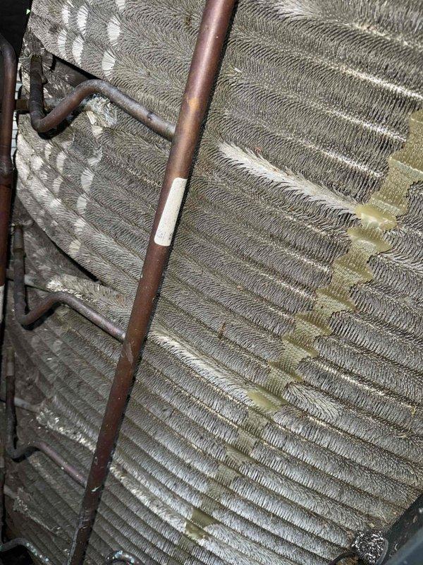 Responded to no cooling call on 10-year-old residential system. Customer has two HVAC units on property. Upon inspection, found evaporator coil exhibiting significant white and yellowish-white buildup and discoloration across fin surfaces, particularly concentrated in upper and middle sections. This contamination was restricting airflow and reducing heat transfer efficiency, resulting in inadequate cooling performance. Both outdoor condenser units located at exterior brick wall appeared in good working condition with clean exteriors and intact components. Documented coil condition with photos showing extensive deposit accumulation on aluminum fins and darkened copper refrigerant lines indicating age and oxidation. System requires coil cleaning or replacement to restore proper cooling operation.