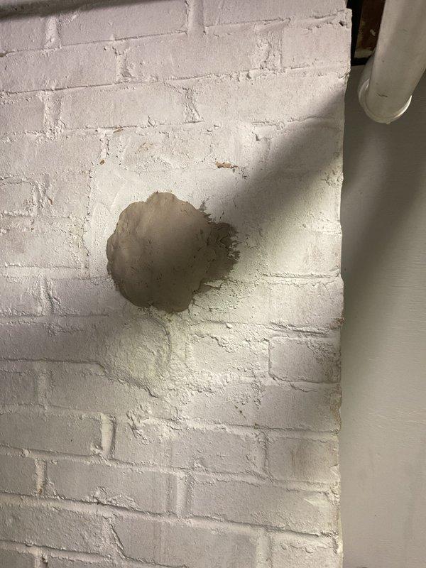Applied high-temperature furnace cement to seal a compromised penetration in the basement utility area where discoloration and paint deterioration indicated heat exposure around a circular opening in the painted brick wall. Supplies were procured and delivered to complete the permanent repair, restoring the integrity of the wall penetration and preventing further heat damage to the surrounding painted surface.