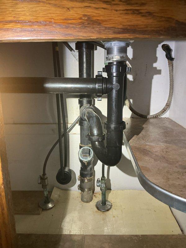 Responded to kitchen sink drain clog. Inspected plumbing assembly beneath sink, including chrome drain pipe, P-trap, and supply lines. Cleared blockage from drain system and verified proper water flow through pipes. All plumbing components functioning properly upon completion.