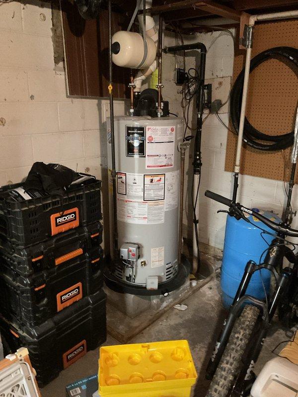 Responded to clogged drain issue near furnace in basement utility area. Upon arrival, found AC unit had been turned off to prevent continued water leakage from the blocked drain line. Assessed the drainage system and identified blockage in condensate drain line. Cleared obstruction from drain line to restore proper water flow and prevent future overflow. Verified drainage system was functioning correctly before restoring AC operation. Documented existing conditions of water heater, surrounding plumbing infrastructure, and work area with photos showing PVC drainage components and basement utility space layout.
