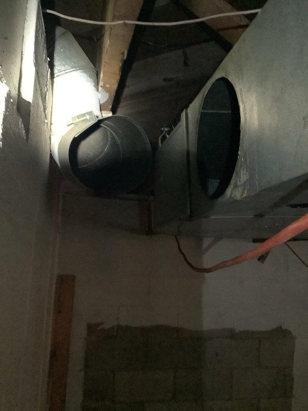 Responded to service call for detached ductwork elbow in basement utility area. Upon inspection, found large cylindrical metal supply duct with disconnected elbow joint. Reattached and secured elbow connection to main duct run, restoring proper airflow through the HVAC system and eliminating potential conditioned air loss into the unconditioned space.
