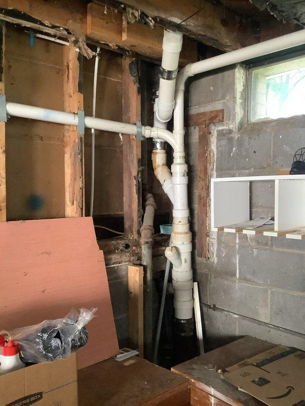 Completed rerouting of sump pump discharge line and shower drain in unfinished basement utility area. Installed new white PVC drainage piping with proper fittings and connections through exposed framing and concrete block walls, ensuring proper pitch and code-compliant installation for effective water removal.