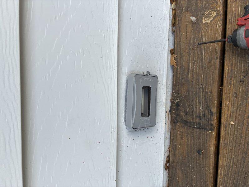 Corrected exterior electrical outlet installation that was previously mounted in improper orientation. Verified weatherproof GFCI outlet box and conduit are now installed to code specifications on building exterior where white siding meets wooden planks. Tested outlet functionality and confirmed proper grounding and weather protection.